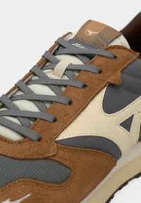 Brown suede and gray mesh sneaker with beige accents, round laces, and a logo on the tongue; textured upper and cushioned sole.