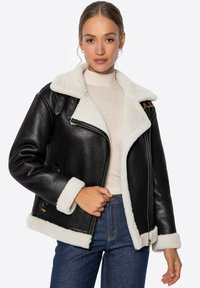 Czarna skórzana kurtka z białym kołnierzem i mankietami z owczej wełny. Posiada zamek z przodu, kieszenie oraz dekoracyjne akcenty ze sprzętu.
