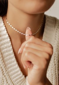 Silberne herzförmige Choker mit einem filigranen Kettendesign, das auf der Haut liegt. Die Hand des Models berührt sanft die Halskette.