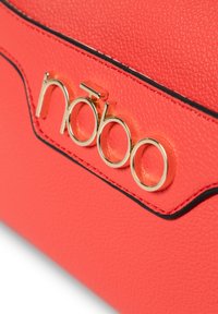 Borsa in pelle sintetica rossa con texture, caratterizzata da un logo dorato e dettagli neri lungo il bordo. Finitura liscia con un design strutturato.