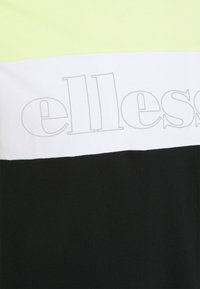Camiseta de manga corta con diseño a bloques de color: amarillo neón, blanco y negro. Presenta un gran logo gris en el centro. Material de algodón.