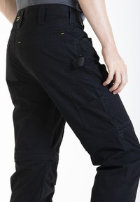 Pantalons de travail noirs au design robuste, avec plusieurs poches, un tissu texturé et des sangles réglables. Renforcés au niveau des genoux.