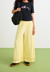 Black cropped t-shirt with mountain graphic, paired with flowing yellow wide-leg pants featuring lace trim, and black shoes with gum soles.
