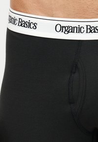 Κοντινό ανδρικού μαύρου εσωρούχου με λευκή ζώνη μέσης που φέρει το κείμενο «Organic Basics» μαύρο.