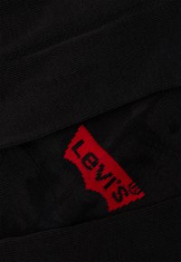 Svarta leggings i en texturerad nyans, med en framträdande röd Levi's-logotyp på en mönstrad lapp. Designen är enkel och strömlinjeformad.