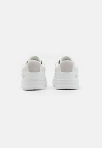 Valged tenniseketid, millel on sile nahk ja sametist pealne, ümar nina, pehmendatud kaelus ja tekstureeritud kummitald. Lacoste logo kandadel.