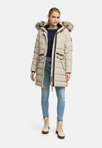Padded beige parka with fur-trimmed hood, featuring black lining, zippered pockets, and an adjustable drawstring at the waist.