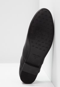 Semelle de chaussure en cuir noir, présentant une texture lisse et des motifs subtils. Le nom de la marque "ANNA FIELD" et la taille "37" sont embossés sur la surface.