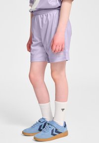 Ljust lila träningsshorts med resårmidja, kombinerat med ljusblå sneakers med en mörkblå sicksackdesign och vita strumpor.