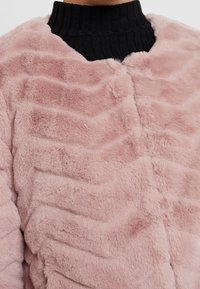 Rosa faux fur-jakke med en ribbet sort krave; har et bølget teksturmønster og rundet frontlukning.
