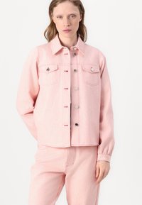 Light pink denim jacket with long sleeves, two front pockets, button closure, and a slightly cropped fit. Textured finish with visible fibers.