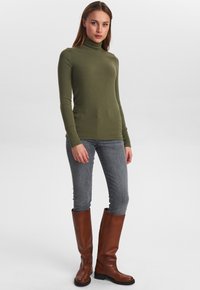 Oliveza zaļa garas piedurknes turtlenecks, šaurs piegriezums. Apvienots ar gaiši pelēkajām džinsām un ceļgalu augstām brūnām ādas zābakiem. Gluda tekstūra, minimāls dizains.