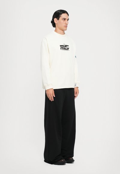 Sweatshirt crem cu croi lejer, având o grafică cu "ITALY", asortat cu pantaloni negri largi și pantofi negri. Textură netedă, design casual.