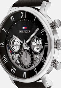 Orologio cronografo nero con cassa in acciaio inossidabile argentato, quadrante intricatamente dettagliato con meccanismi visibili, numeri romani e cinturino in pelle.