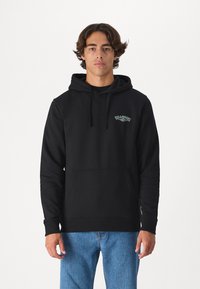 Black hooded sweatshirt made of cotton blend, featuring a front pocket and embroidered logo on the chest. Paired with light blue jeans.