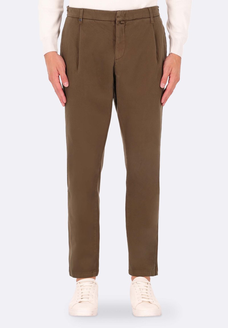 Pantaloni marroni in cotone misto, con davanti piatto, due tasche frontali e design slim fit, abbinati a scarpe da tennis bianche.