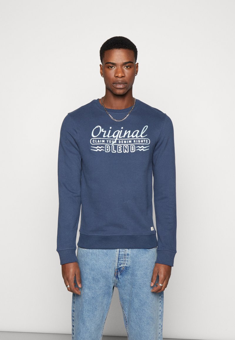 Mornarsko plavi dukserica s rebrastim manžetama i rubom, koja na prsima ima bijeli natpis "Original Claim Your Denim Rights Blend".