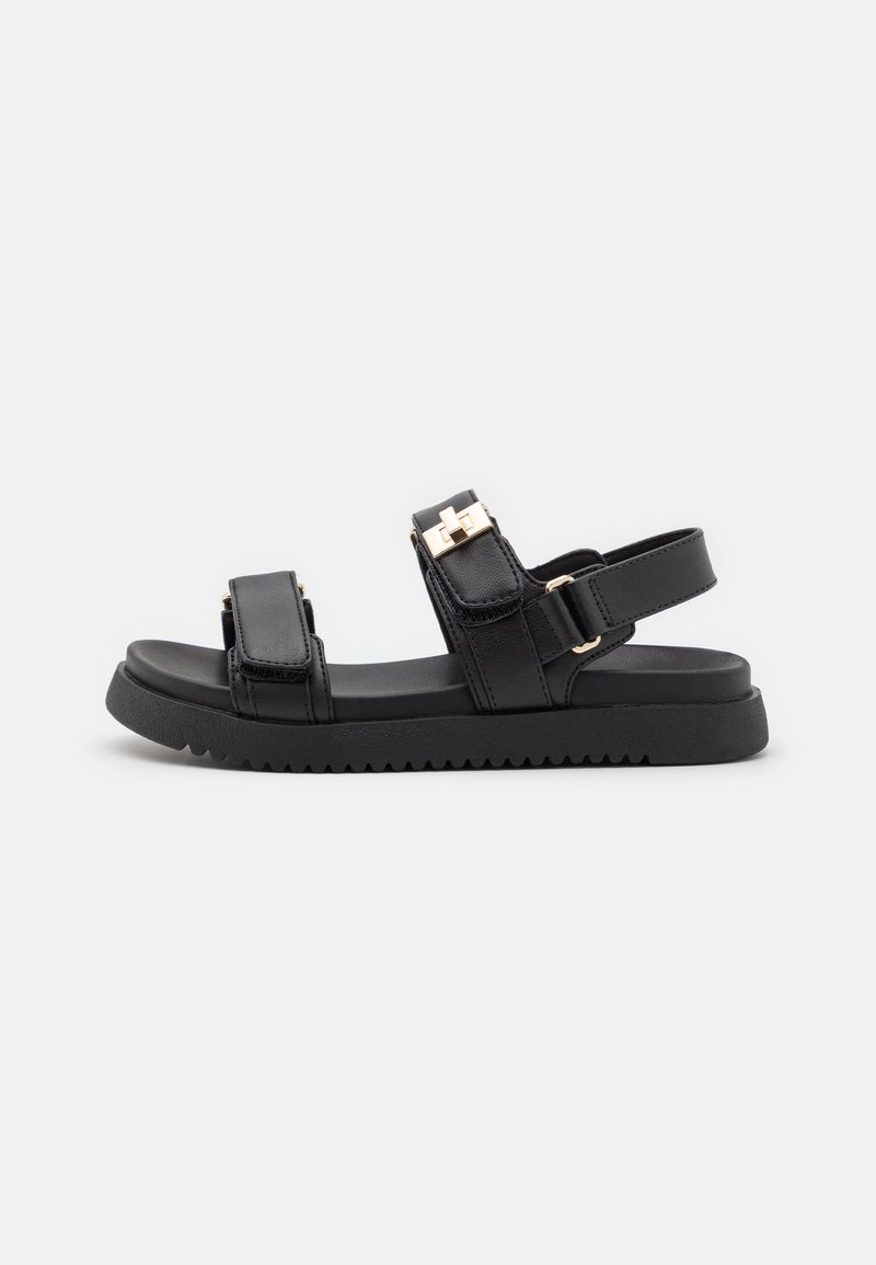 Zwarte platte sandalen met twee verstelbare riemen, gemaakt van gestructureerd leer, voorzien van een contrasterende gouden accent en een gegroefd rubberen zool.