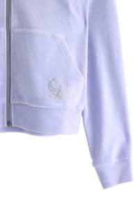 Fioletowa bluza z kapturem na zamek z miękkiego materiału, z przednią kieszenią i wyhaftowanymi srebrnymi cyrkoniami inicjałami po lewej stronie.