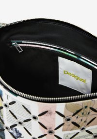 Reißverschlussbeutel mit einem schwarzen Innenraum, der eine gemusterte Außenseite mit floralen Designs und Metallösen aufweist. Markenlabel innen: "Desigual."