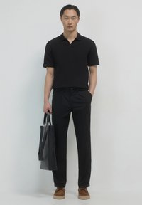 Schwarzes Polohemd, maßgeschneiderte schwarze Hose, braune Schuhe und eine schwarze Tote-Tasche. Das Outfit zeichnet sich durch klare Linien und ein minimalistisches Design aus.