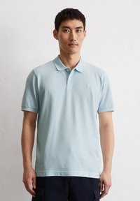 Hellblaues Poloshirt mit weicher Textur, kurzen Ärmeln und klassischem Kragen. Mit dezenter Markenkennzeichnung und kontrastierenden Knöpfen.