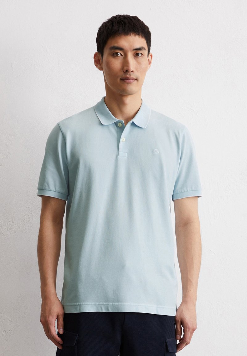 Hellblaues Poloshirt mit weicher Textur, kurzen Ärmeln und klassischem Kragen. Mit dezenter Markenkennzeichnung und kontrastierenden Knöpfen.