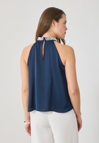 Sötétkék pánt nélküli felső, kulcslyuk hátkivágással és gyöngyös nyakkivágással, sima, könnyű anyagból készült. Bő szabású, ívelt aljjal.