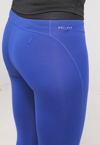 Zbliżenie na osobę w jasnoniebieskich legginsach Dri-FIT i czarnej bluzce, ukazujące teksturę materiału oraz szczegóły szwów.