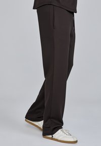 Black athletic pants made of smooth fabric, featuring a relaxed fit, side pockets, and tapered cuffs, paired with white sneakers.