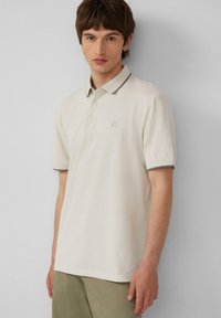 Lichtbeige poloshirt met een kraag, drieknopen-sluiting en grijze rand bij de kraag en mouwen; geborduurd logo op de borst.