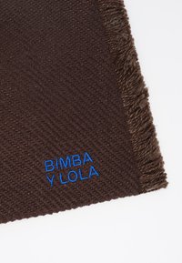 Bruine geweven sjaal met franjes aan de randen, met "BIMBA Y LOLA" geborduurd in het blauw. De textuur lijkt zacht en dik te zijn.