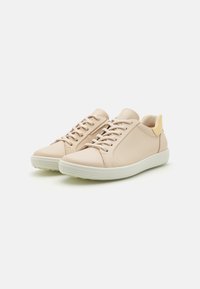 Beige Leder-Sneaker mit glatter Oberfläche, flachen weißen Gummisohlen, Schnürdesign und einem kontrastierenden gelben Akzent an der Ferse.
