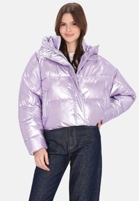 Lilla pufferjakke med en blank, quiltet tekstur, med høj krave, lynlås foran og lommer. Kombineret med mørke denimjeans.