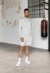 Grijze sweatshirt en shorts van een katoenmix, met een logo op de borst. Witte sneakers en sokken maken de sportieve look compleet.