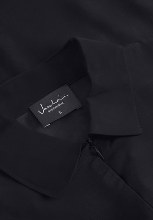 Bluză neagră cu un guler clasic, având o textură subtilă, fermoar pe lateral și un etichetă care arată marca "Vascha" și mărimea "S."