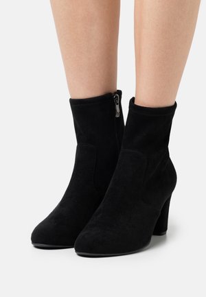 Botines de ante negro con tacón cuadrado, que cuentan con una cremallera lateral y una textura suave, diseñados con una silueta ajustada y punta afilada.