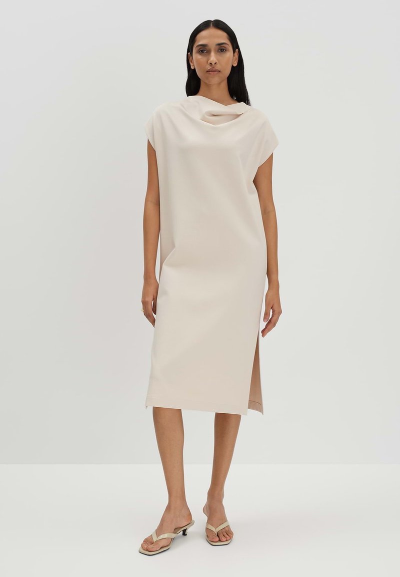 Cowl Neck Midi-Kleid in Hellbeige, mit kurzen Ärmeln, Seitenschlitz und glattem Stoff in lockerer Passform, kombiniert mit minimalistischen flachen Sandalen.