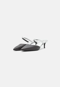 Talons slingback en synthétique noir avec des orteils pointus et une bride en argent brillant. Présente un talon mince et une texture lisse.