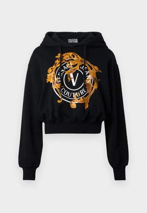 Svart kort hoodie laget av mykt stoff, med et gyllent og oransje ornamentert grafikk som har sirkulær tekst og et sentralt "V"-logo.