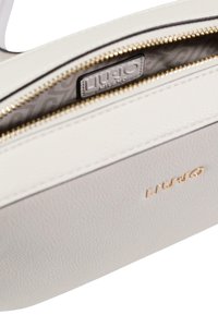 Borsa in pelle beige chiaro con texture, dotata di una cerniera dorata, che mostra un interno decorato da un motivo e una piccola etichetta con il logo all'interno.