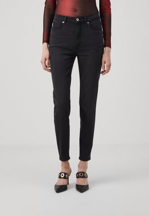 Jean slim noir porté avec des escarpins noirs à bout pointu comportant de larges brides avec des œillets dorés.