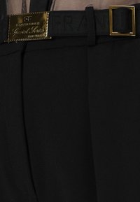 Pantaloni neri con texture liscia, caratterizzati da una cintura ampia con fibbia color oro e marchio stampato.