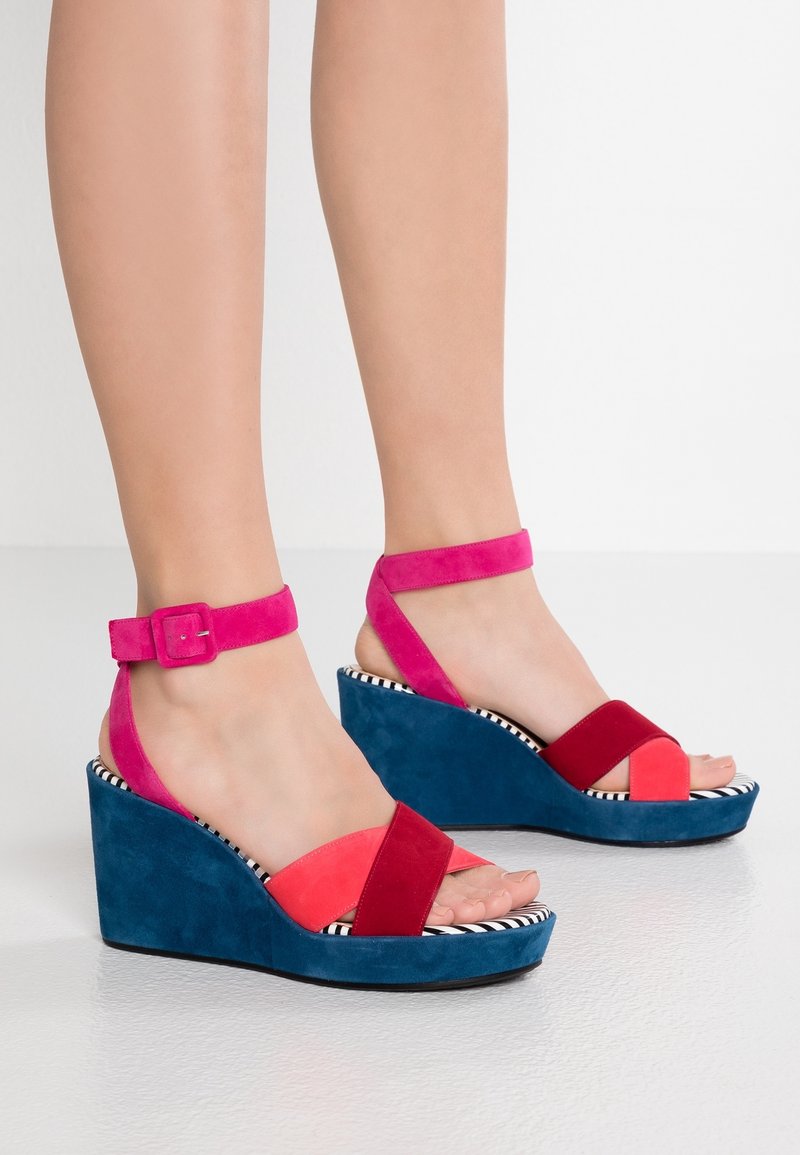 Sandales compensées colorées en daim rose, rouge et bleu, avec un design à lanières croisées et un motif intérieur rayé. Brides de cheville ajustables.