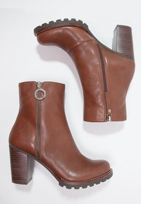 Bottines en cuir marron avec un talon épais, une fermeture éclair sur le côté et une semelle texturée. Finition lisse et détail de tirette de fermeture éclair circulaire.