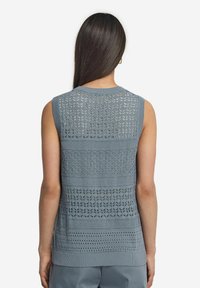 Ärmlös stickad topp i blått med texturerade mönster, med en blandning av solid och öppen väv. Sytt halsringning och fåll detaljer.