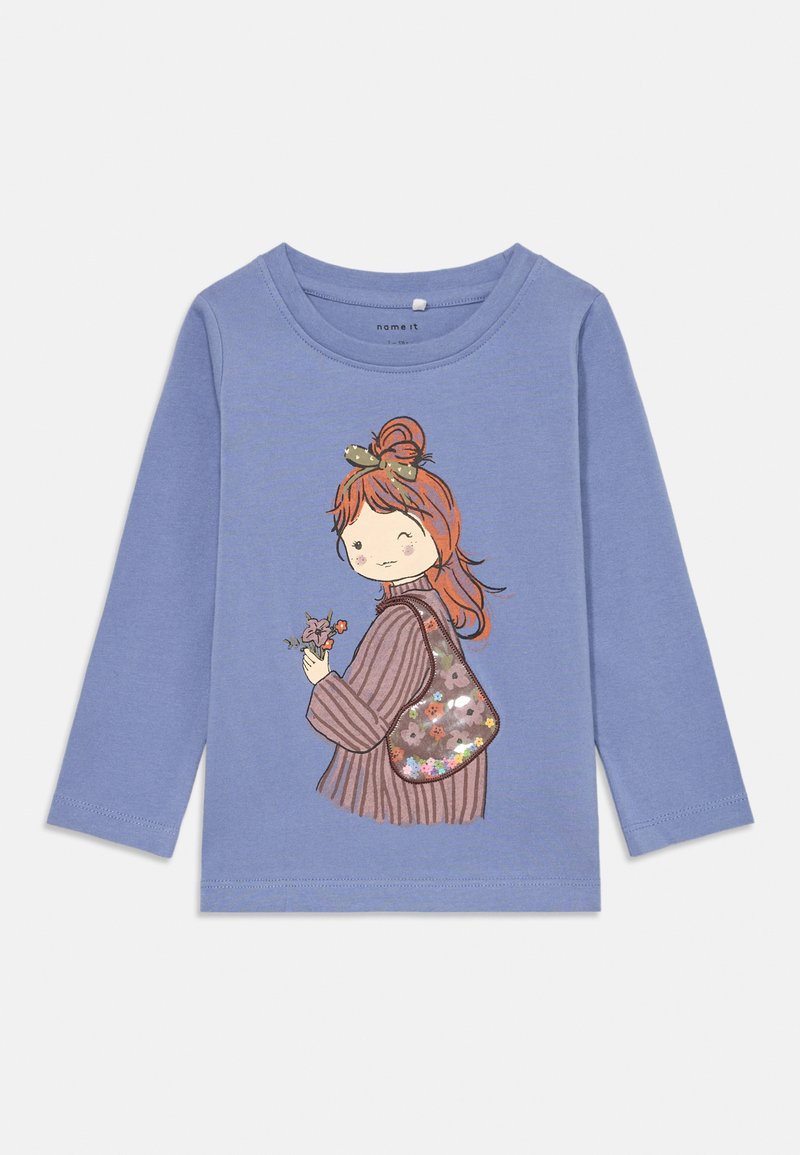 Μπλε πουκάμισο με μακριά μανίκια που διαθέτει γραφικό σχέδιο μιας κοπέλας με καστανά μαλλιά, που κρατά λουλούδια και μια τσάντα με μοτίβο, από απαλό βαμβακερό ύφασμα.