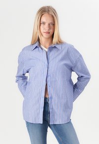 Camicia a bottoni a strisce blu con righe verticali, in contrasto con sottili righe bianche e rosse. Maniche lunghe, vestibilità rilassata e colletto classico.
