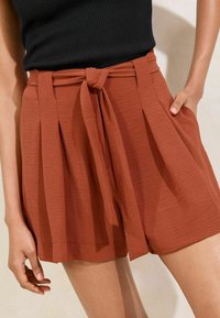 Roodbruine shorts met een strikband, geplooid ontwerp en zijzakken, gemaakt van een lichtgewicht, gestructureerde stof.