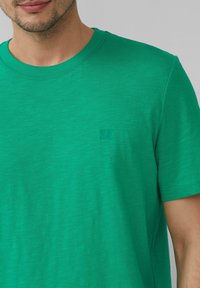 Zielony bawełniany t-shirt z okrągłym dekoltem i krótkimi rękawami, z subtelnym logo nadrukowanym na piersi. Gładka faktura i lekki materiał.